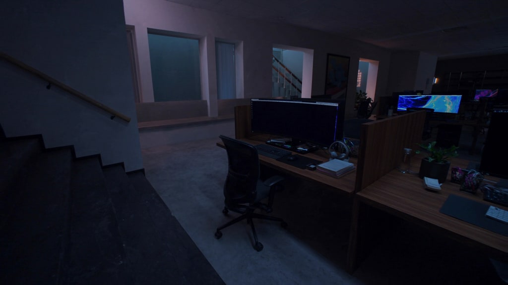 Computer workstations with monitors and office chairs beside a staircase.
