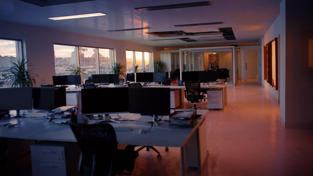 Rows of desks and computer monitors in an open-plan office at sunset.